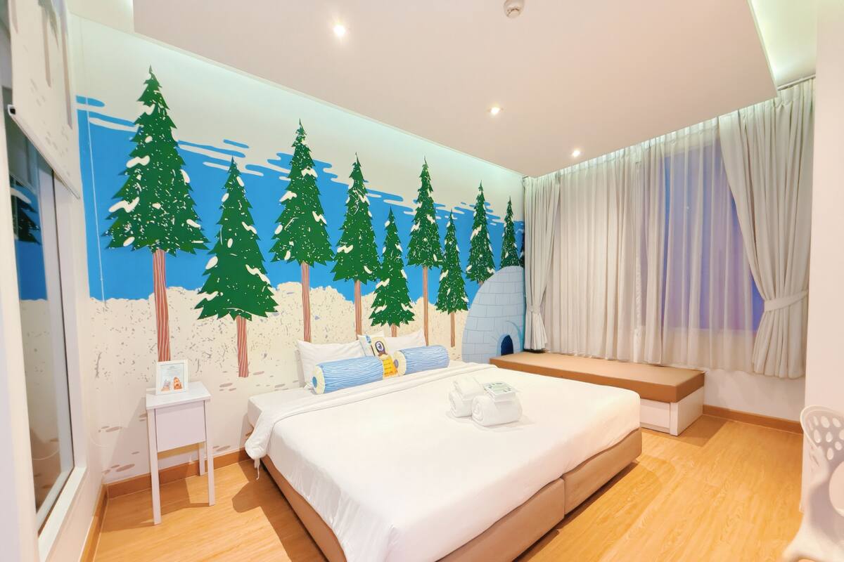 Une chambre à coucher avec un grand lit, une table de chevet, une commode, une fenêtre avec des rideaux et une fresque murale représentant des arbres.