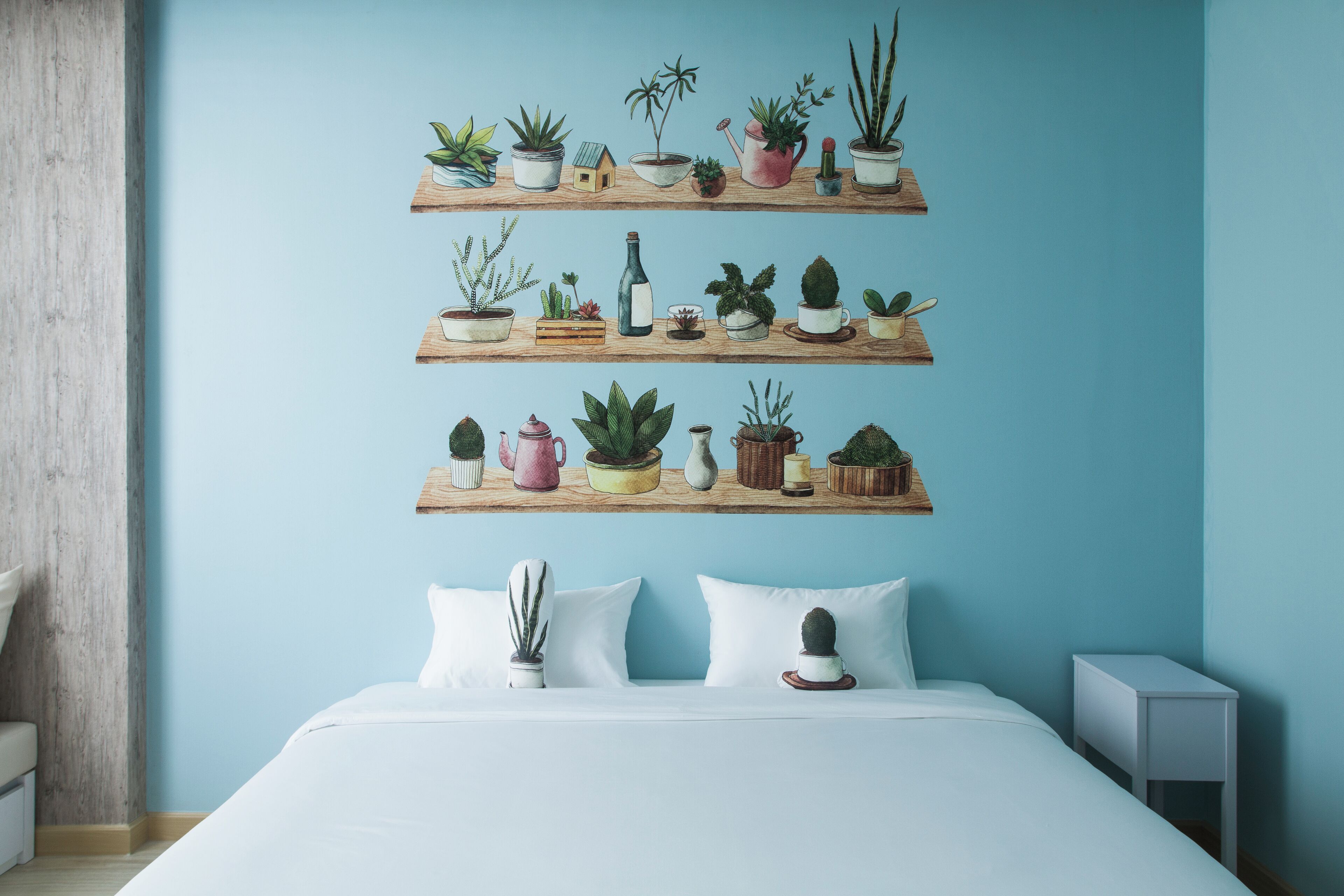 Un dormitorio con una cama, almohadas blancas y tres estantes de madera con diversas plantas en macetas.