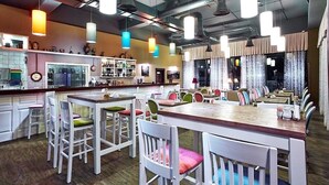 Um restaurante com várias mesas e cadeiras, uma área de bar e uma cozinha visível ao fundo.