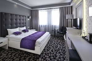 A modern hotel room with a large bed, a desk, a chair, a TV, and a window with curtains. - Hotel Manufactura (Khodosivka)