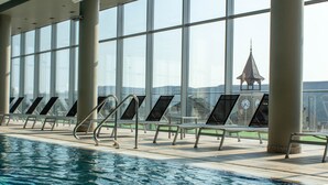 Piscina interna com vista clara para uma torre distante através de grandes janelas.