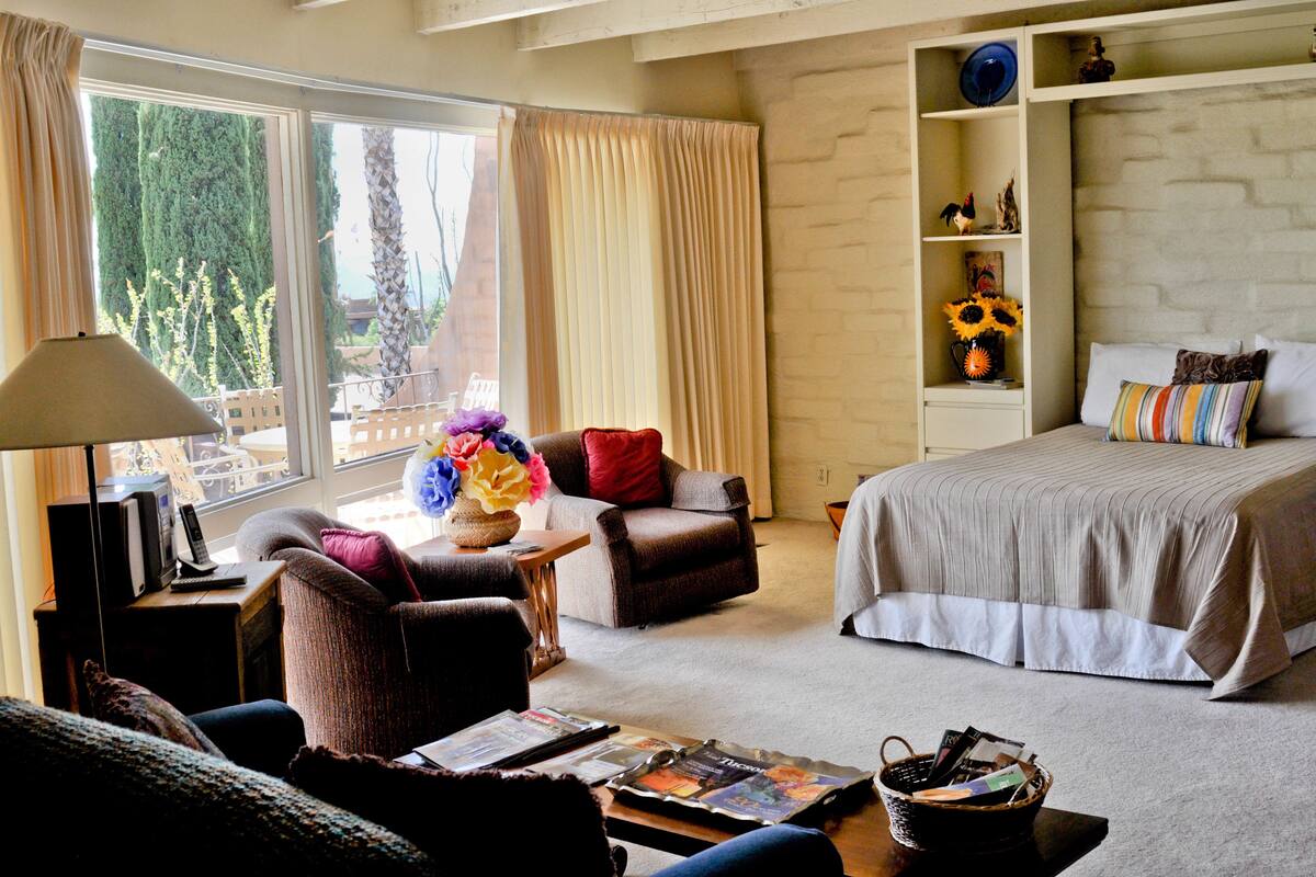 Ein Schlafzimmer mit Bett, Stuhl, Schreibtisch und einem Fenster mit Vorhängen.