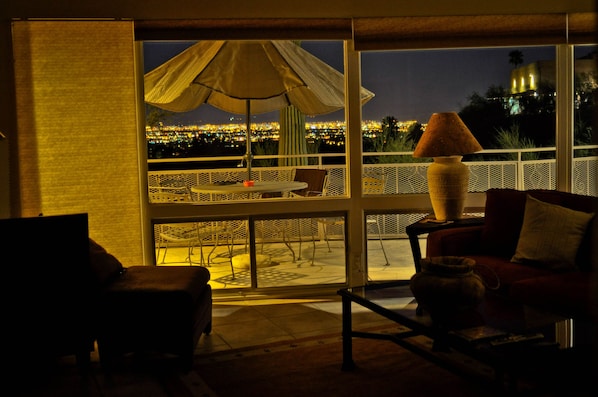 A room with a large window overlooking a cityscape at night, a table with chairs, and a sofa.