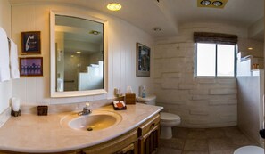 A bathroom with a large mirror, a sink, a toilet, and a window.