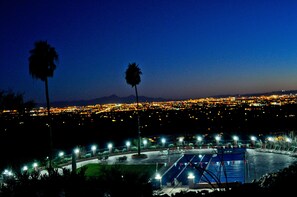 A nighttime view of a cityscape with a well-lit parking area and two palm trees.