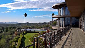 A modern building with large windows and a balcony overlooking a landscaped area with a view of distant mountains. - Mission Hill Casitas (Tucson)