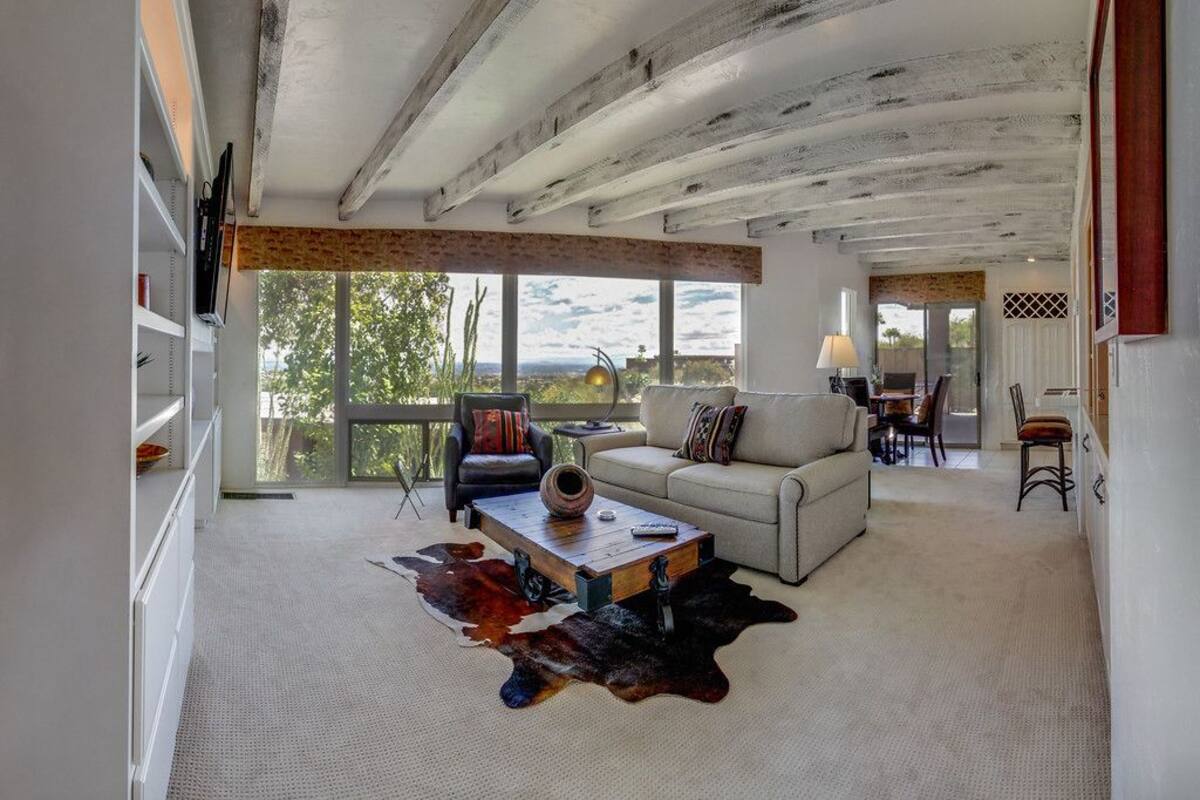 Ein geräumiges Wohnzimmer mit hohen Decken, einer Couch, einem Couchtisch und einem großen Fenster mit Blick ins Freie.