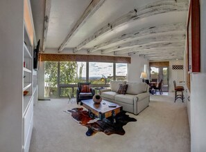 Un salon spacieux avec un plafond haut, un canapé, une table basse et une grande fenêtre donnant sur l’extérieur.