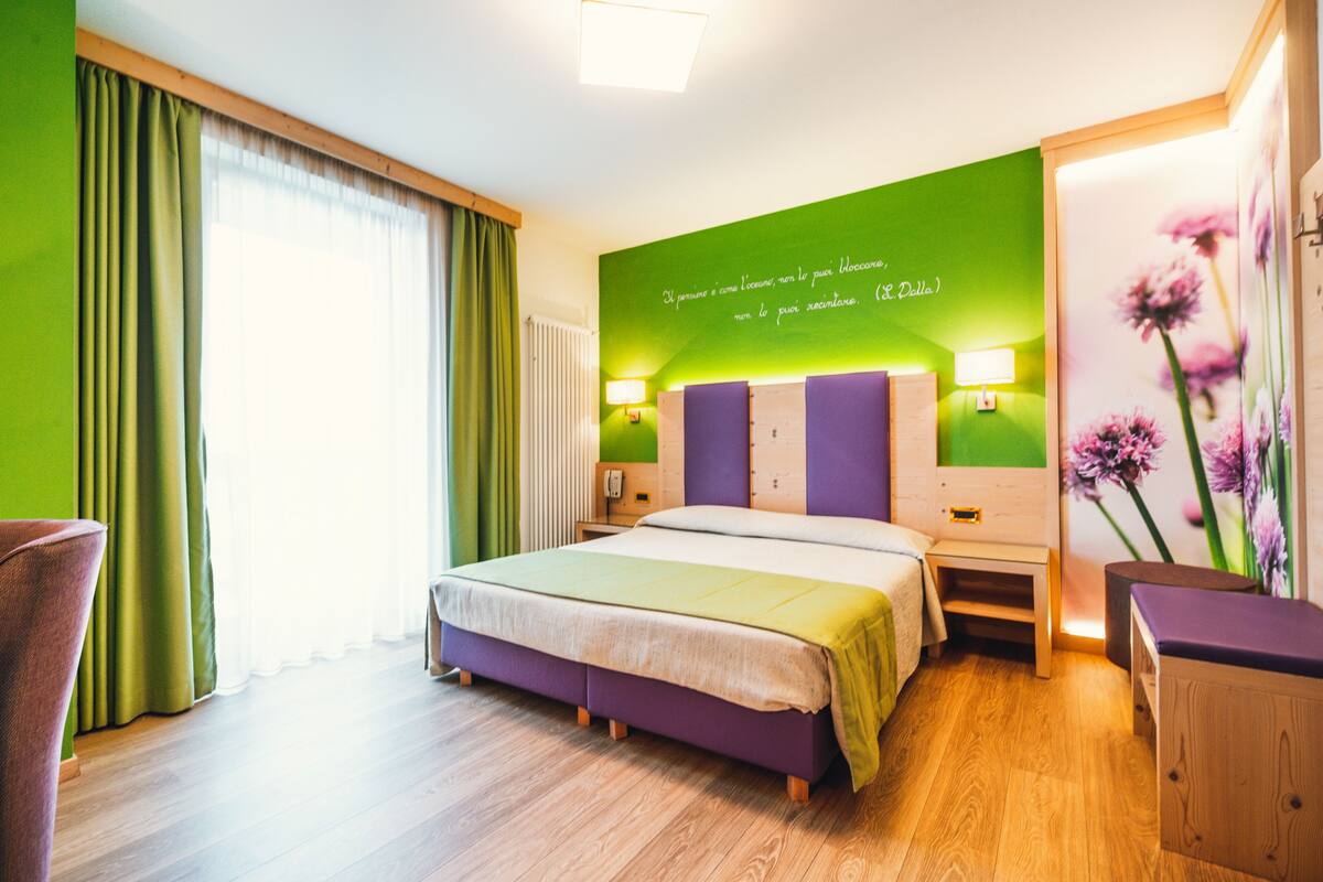 Une chambre d’hôtel avec un lit, une table de chevet, une lampe, une chaise et un mur orné d’une citation.