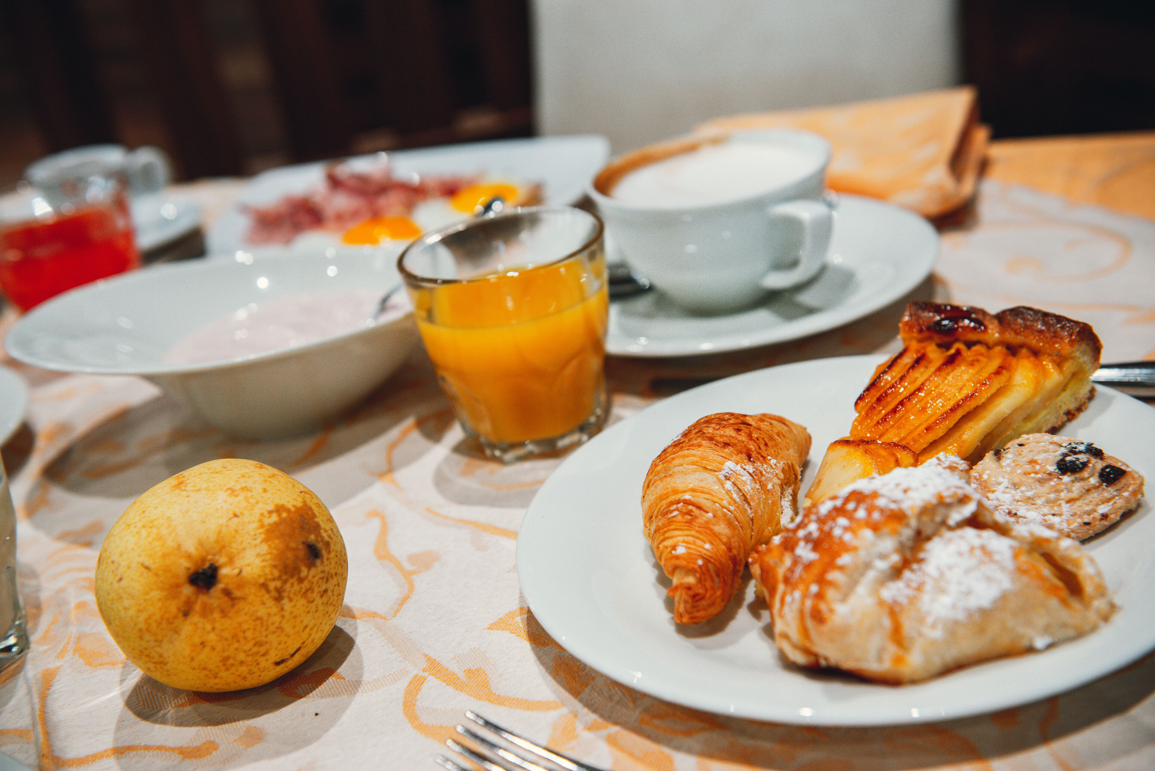 Une table mise pour le petit-déjeuner, avec des croissants, du jus d’orange et un saladier de fruits.
