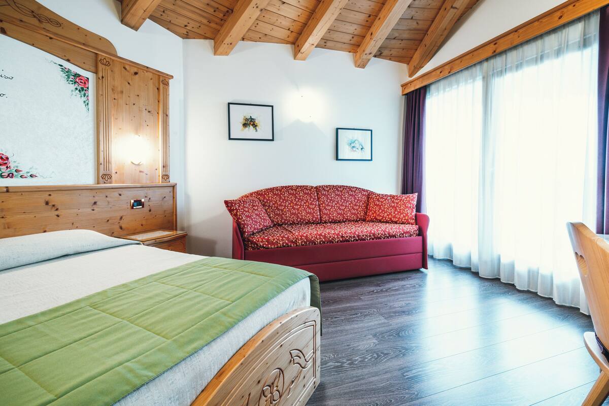Une chambre à coucher avec un lit, un canapé rouge, des poutres en bois au plafond et deux tableaux encadrés accrochés au mur.