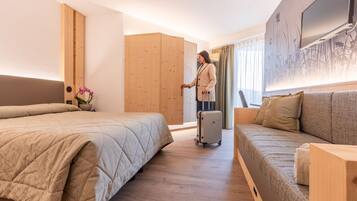 Habitación de hotel con cama, sofá, armario de madera, maleta y televisor en la pared.