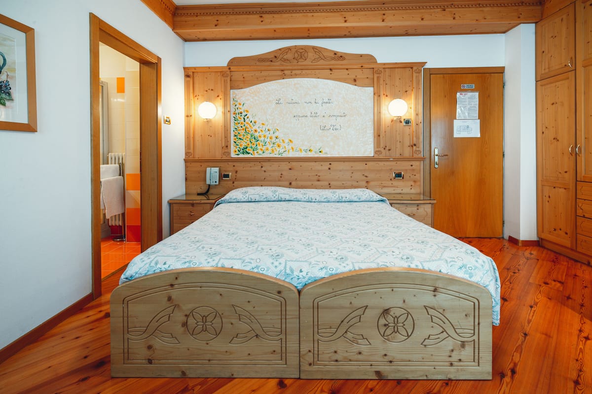 Une chambre à coucher avec une tête de lit en bois, un lit recouvert d’une literie à motifs, une table de chevet et un miroir fixé au mur.