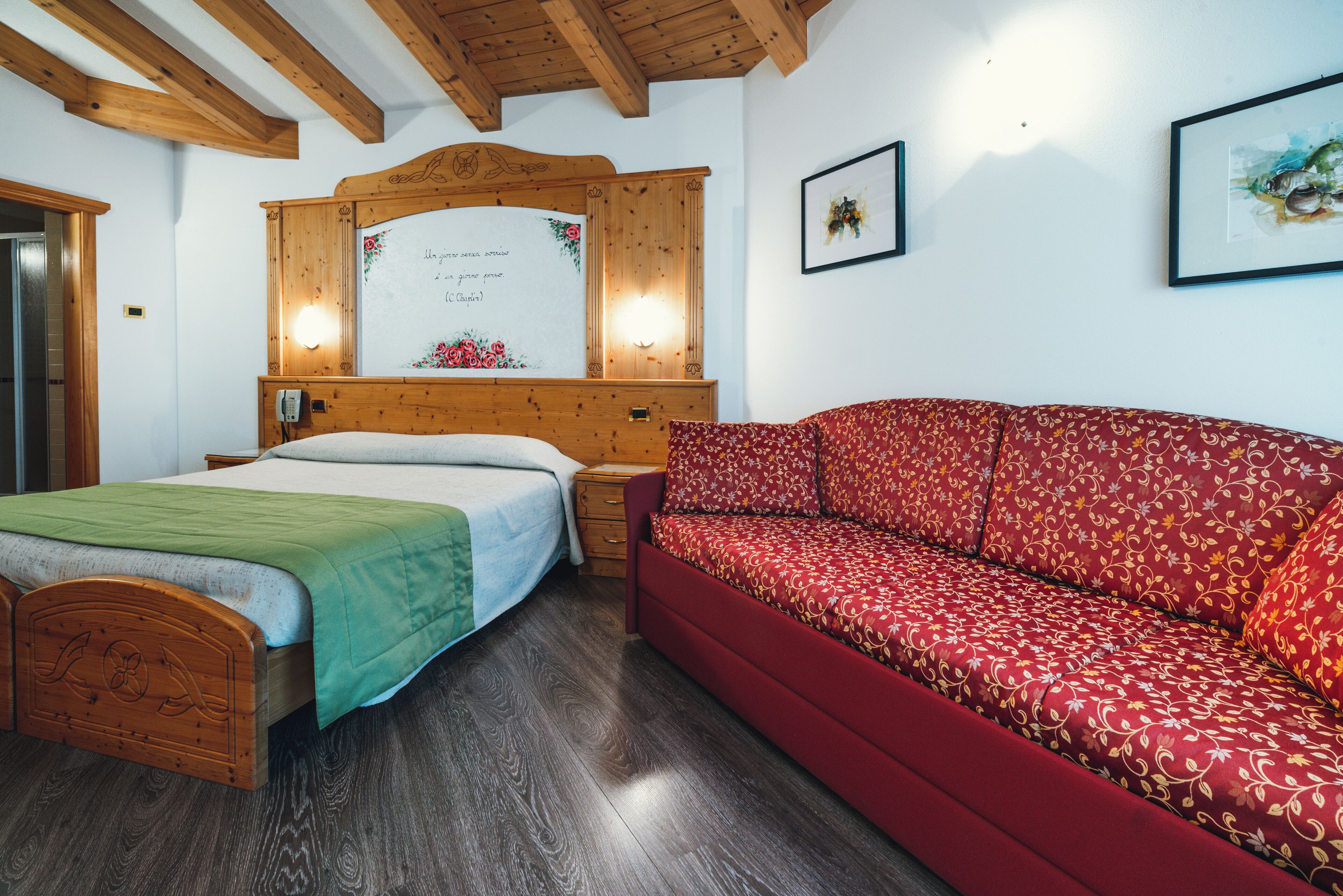 A room with a wooden bed, a red sofa, a wooden headboard, and a wall-mounted light fixture.