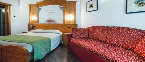 A room with a wooden bed, a red sofa, a wooden headboard, and a wall-mounted light fixture.