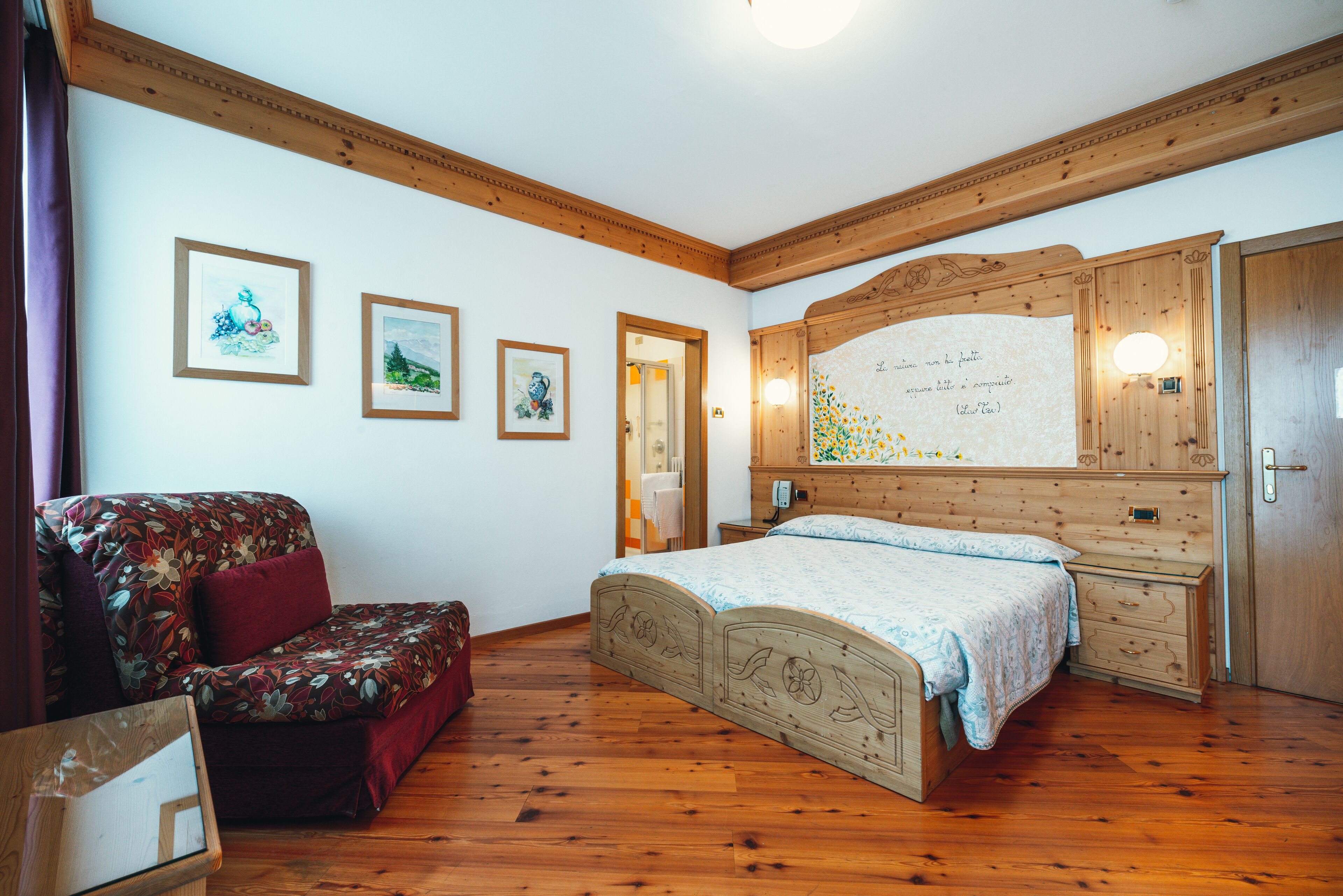 Ein Schlafzimmer mit einem hölzernen Bett, einer Kommode aus Holz, einer Holzbank und gerahmten Bildern an der Wand.