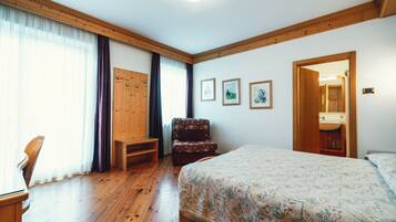 Ein Schlafzimmer mit Holzboden, einem Bett, einem Sessel, einem Schreibtisch und einer Tür zu einem Badezimmer.