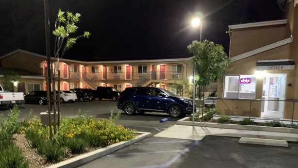 A parking lot with several cars, a building with an 'OFFICE' sign, and a well-lit entrance. - Desert Inn Motel (Corona)