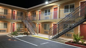 A multi-story motel with a central staircase, individual room entrances, and a parking area marked "COMPACT." - Desert Inn Motel (Corona)