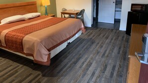 A hotel room with a bed, a desk, a chair, and a door leading to a bathroom. - Desert Inn Motel (Corona)