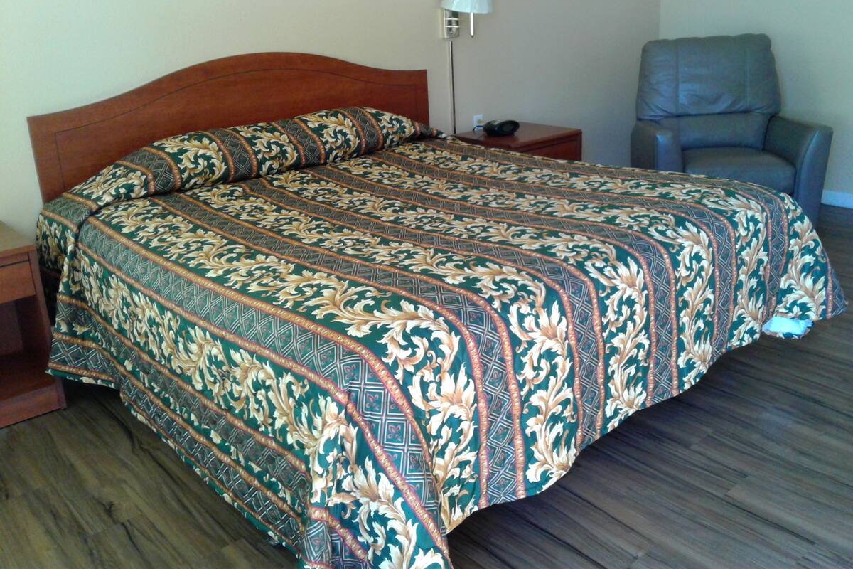 A bedroom with a wooden headboard, a patterned bedspread, a bedside lamp, and a chair.