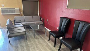 A room with a grey sofa, two black chairs, a glass coffee table, and a red wall. - Desert Inn Motel (Corona)