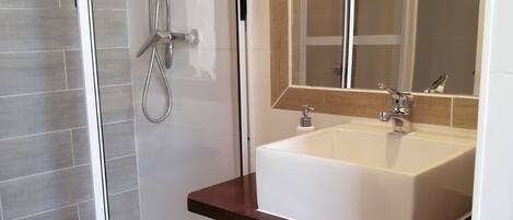 A modern bathroom with a glass-enclosed shower, a white sink with a wooden countertop, and a mirror above the sink.