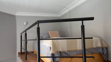Una cama litera con plataforma de madera y barandillas metálicas, un colchón gris y una manta color beige.