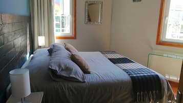 Une chambre à coucher avec un lit, une lampe de chevet, un miroir et une fenêtre avec des rideaux.