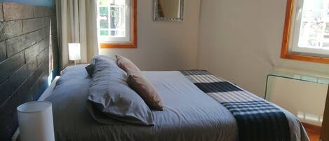 A bedroom with a bed, a bedside lamp, a mirror, and a window with curtains.