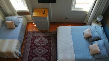 Un dormitorio con una cama, una mesita de noche de madera, un televisor montado en la pared y una ventana con cortinas.