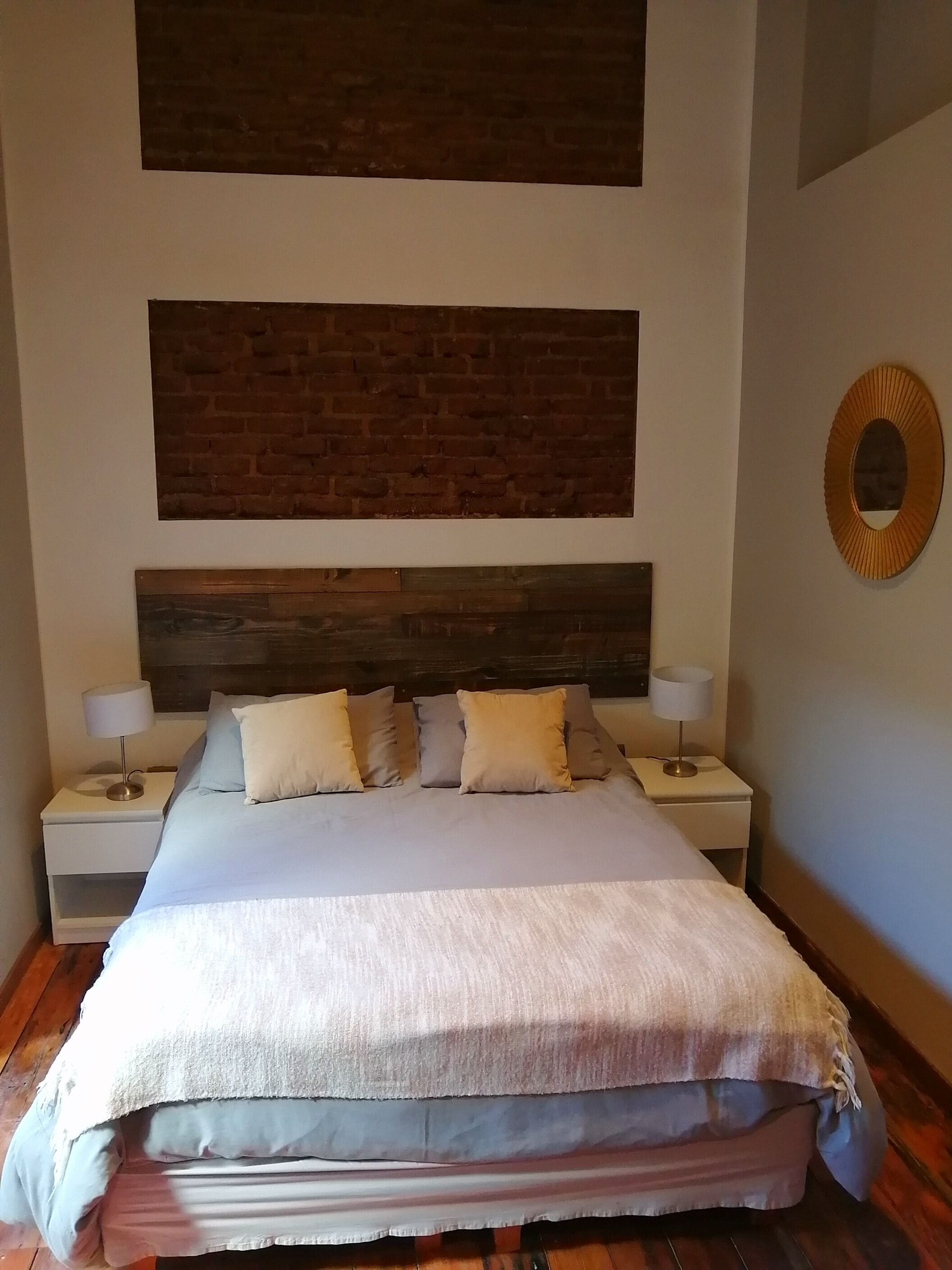 Une chambre à coucher avec un grand lit, deux tables de chevet, une tête de lit en bois et un miroir au mur.