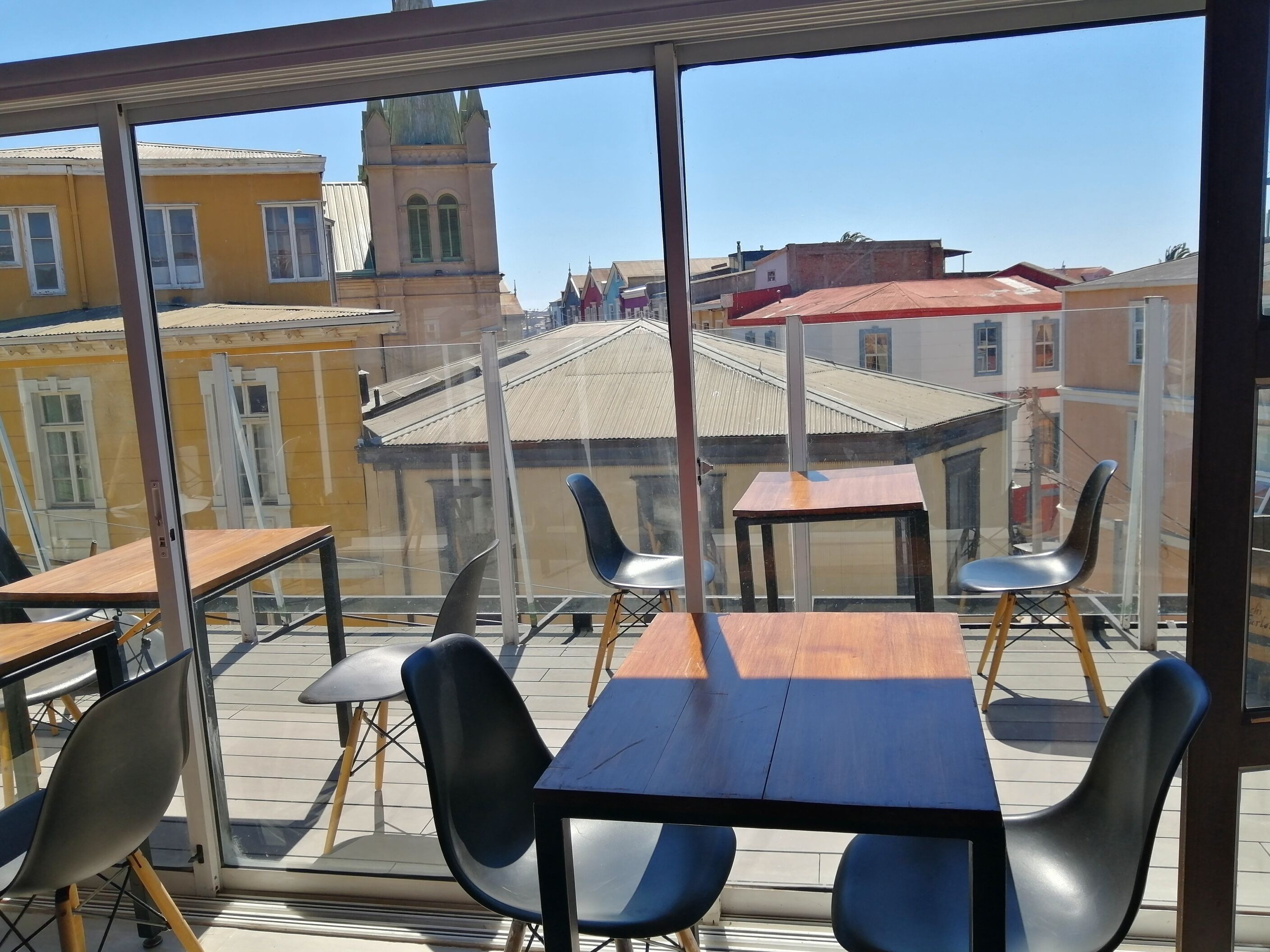 Un espace repas avec des tables et des chaises, de grandes fenêtres offrant une vue sur les bâtiments et une tour.