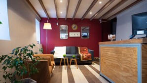 Uma sala de estar aconchegante com parede vermelha, vigas de madeira no teto, um sofá, uma mesa de centro e um vaso com planta.