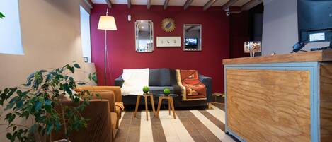 Een gezellige woonkamer met een rode muur, houten balken in het plafond, een bank, een salontafel en een potplant.