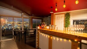 Uma área de bar com vista para a cidade, um espaço de refeições com cadeiras e uma porta com uma planta.