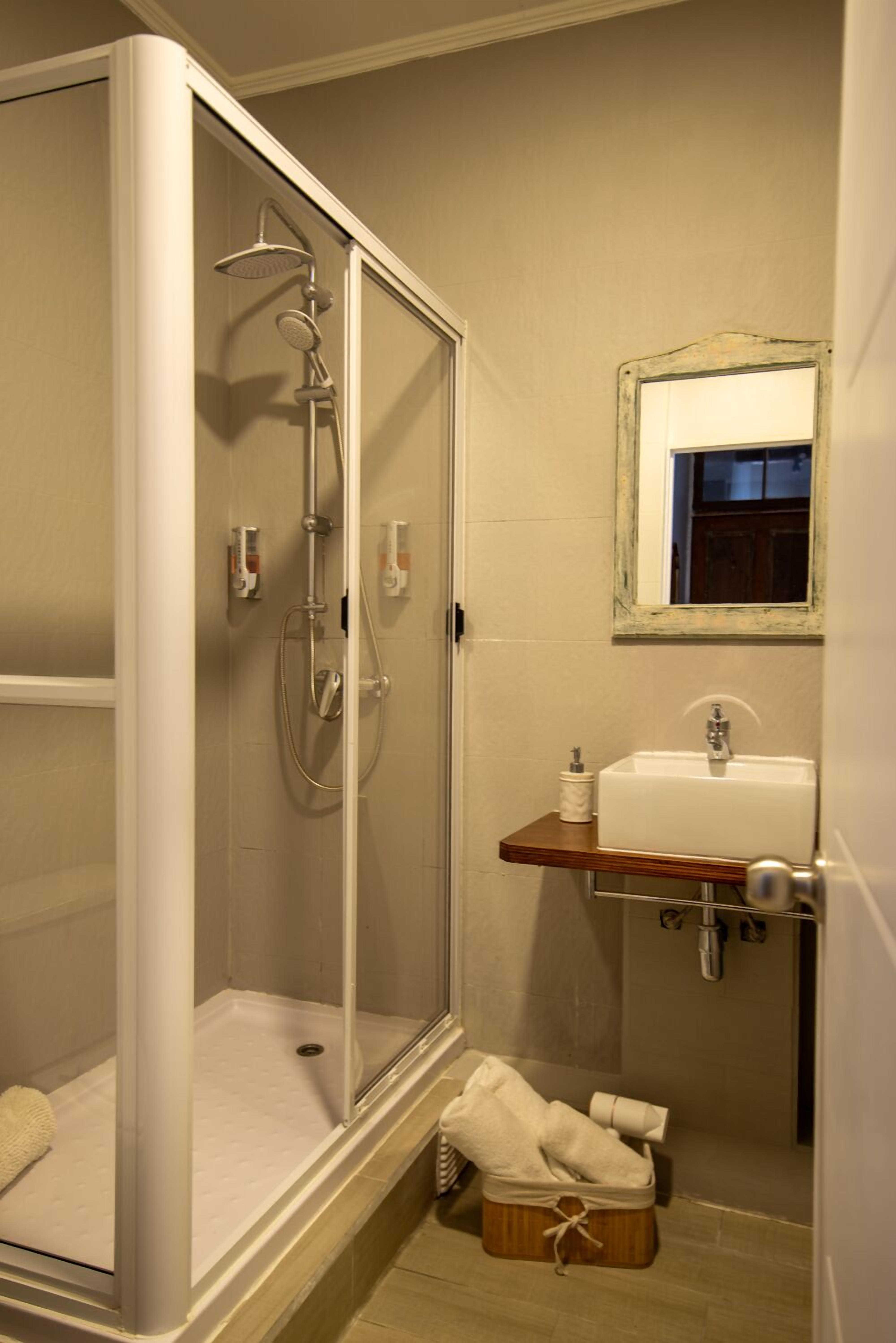 Une salle de bain avec une douche à parois de verre, un lavabo avec un miroir au-dessus et un porte-serviettes.