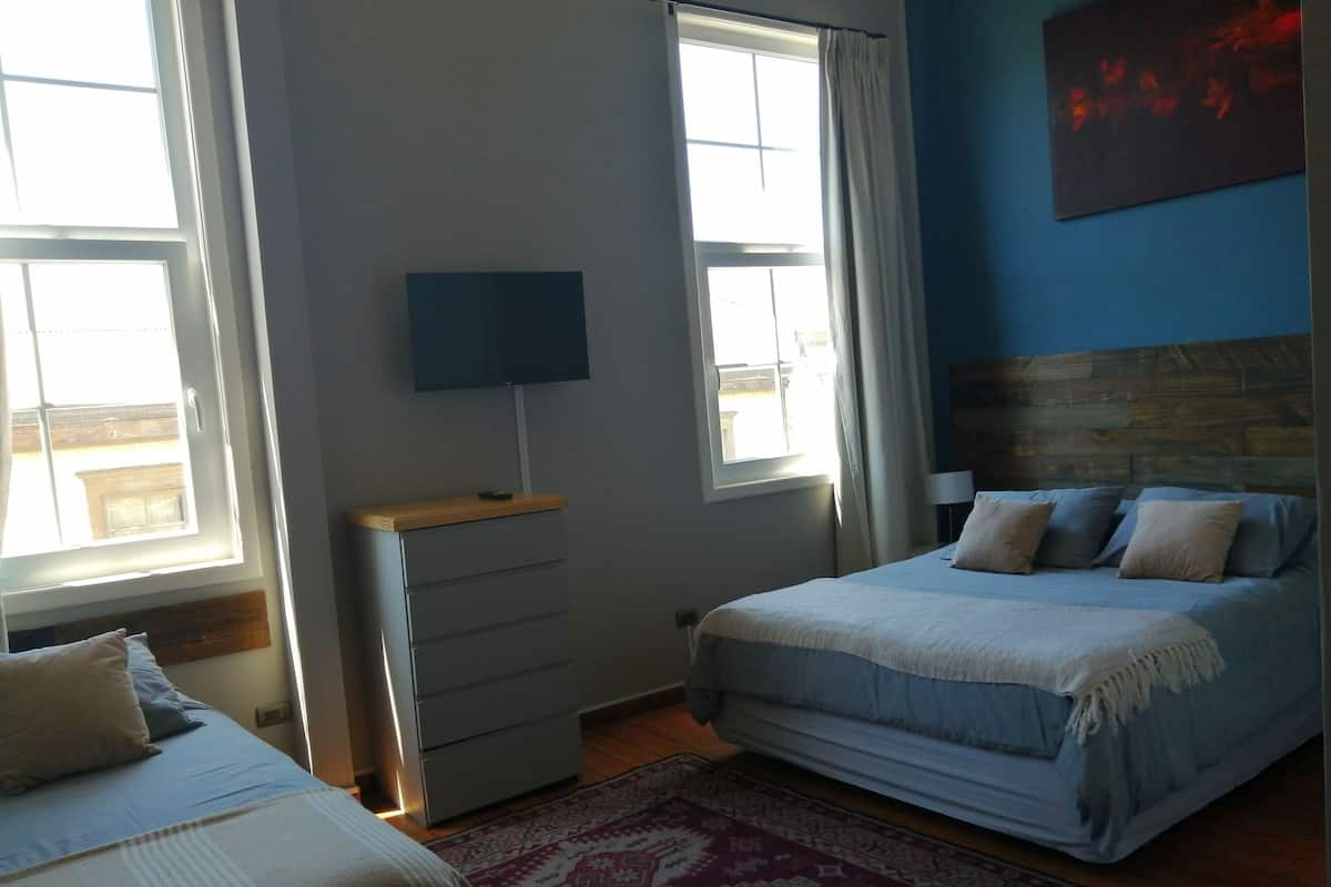 A bedroom with two beds, a dresser, a TV, and a window with curtains.