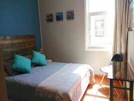 Ein Schlafzimmer mit einem hölzernen Kopfteil, einem Bett mit türkisfarbenen Kissen, einem Nachttisch mit Lampe und einem Fenster mit Vorhängen.