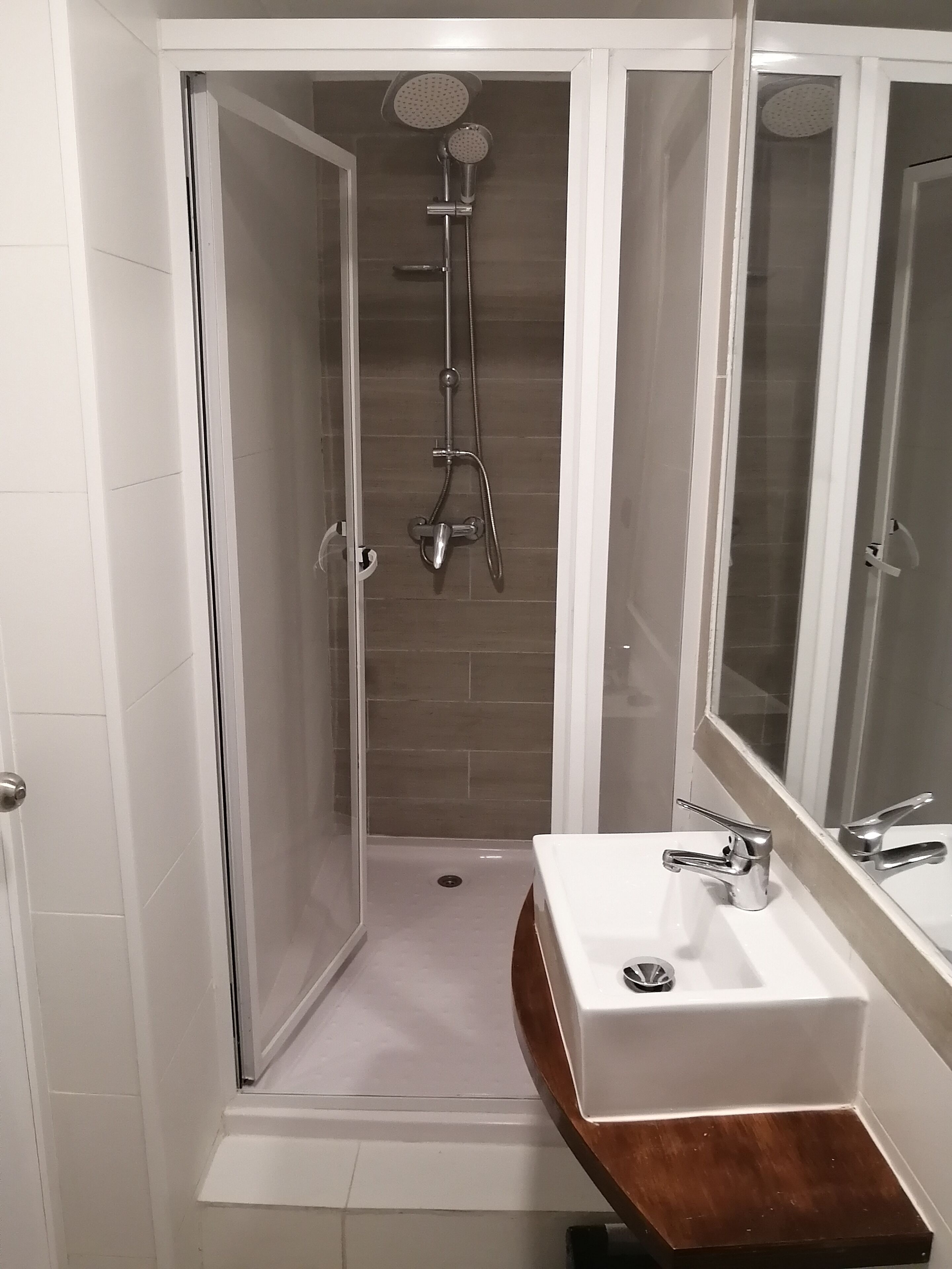 A walk-in shower with a glass door, a white sink with a wooden countertop, and a mirror above the sink.