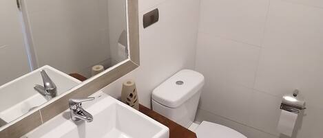 A modern bathroom with a white sink, mirror, and toilet.