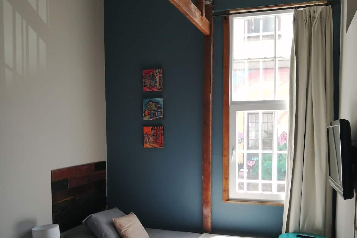 A bedroom with two beds, a window with curtains, a small table, and a TV mounted on the wall.