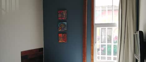 Un dormitorio con dos camas, una ventana con cortinas, una mesita y un televisor montado en la pared.