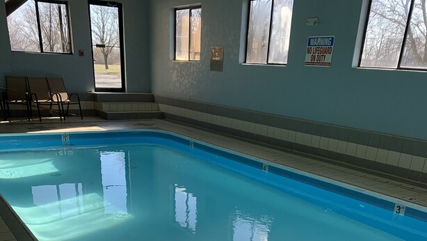 Une piscine intérieure à l’eau claire, avec des couloirs de nage délimités et un panneau d’avertissement indiquant la présence d’un sauveteur.