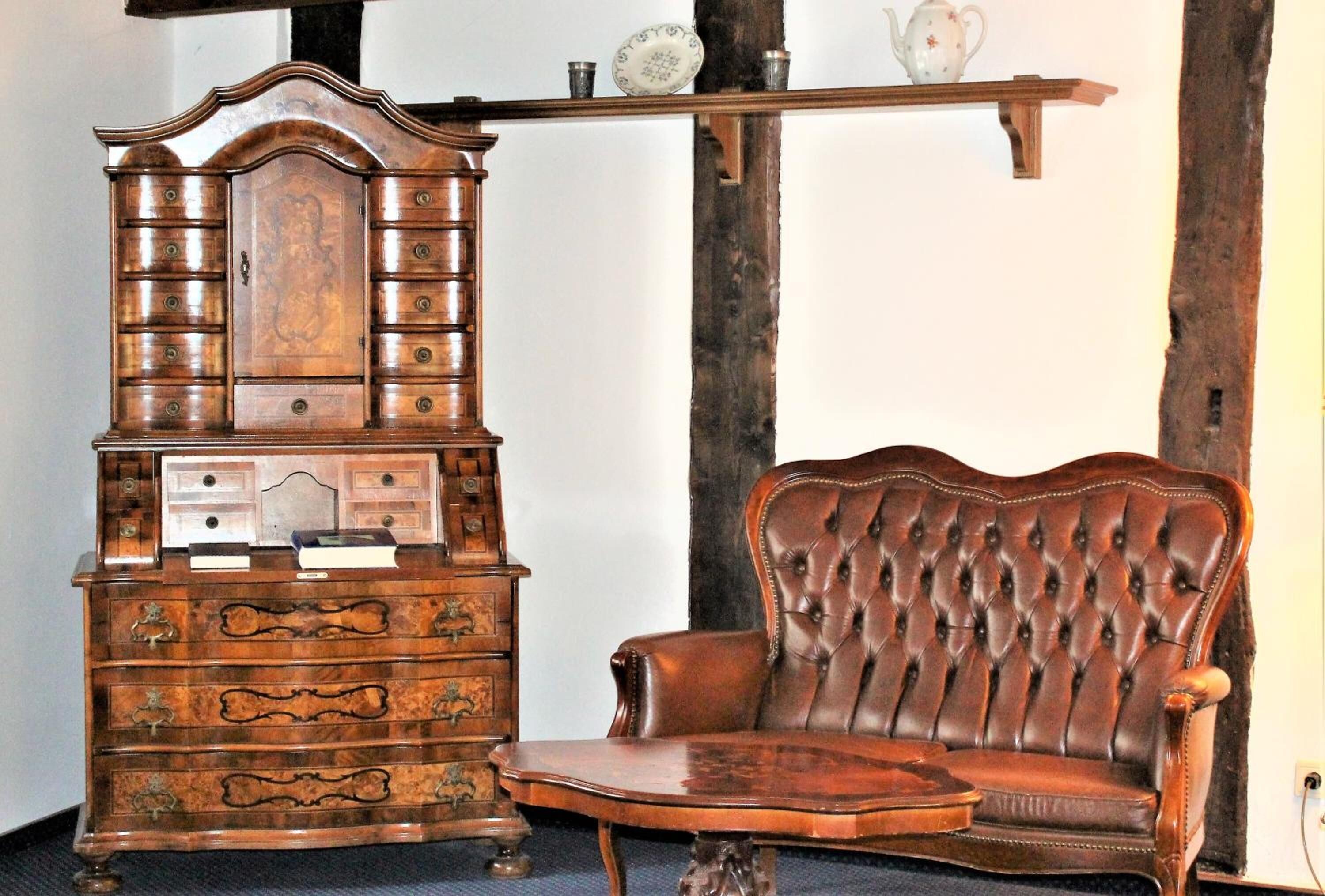 A wooden cabinet with multiple drawers and a cushioned chair with a high backrest.