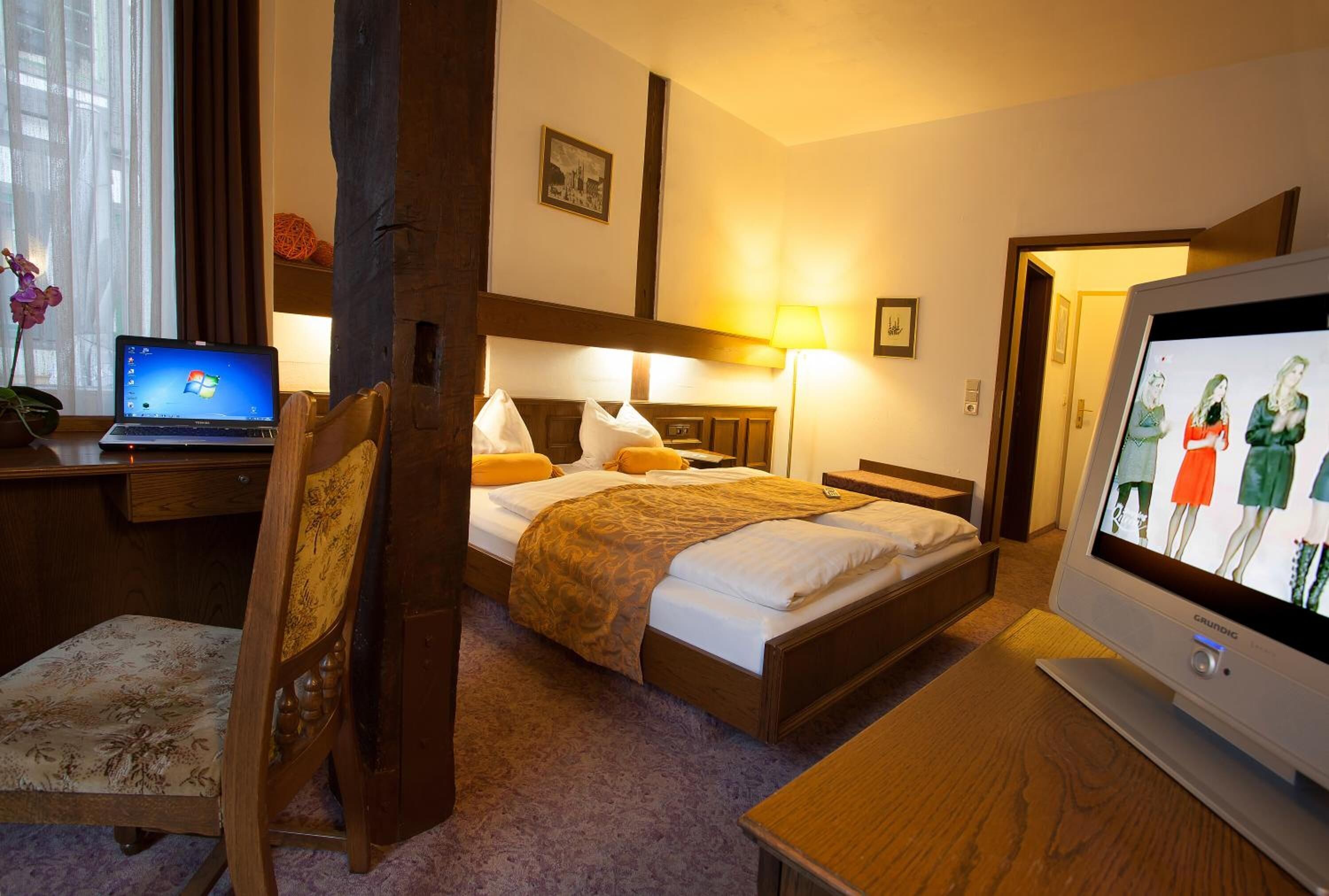 Ett hotellrum med en säng, ett skrivbord med en bärbar dator, en tv och en stol.