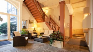 Uma sala de estar ampla com piso de pedra, escada de madeira e vista para o exterior.