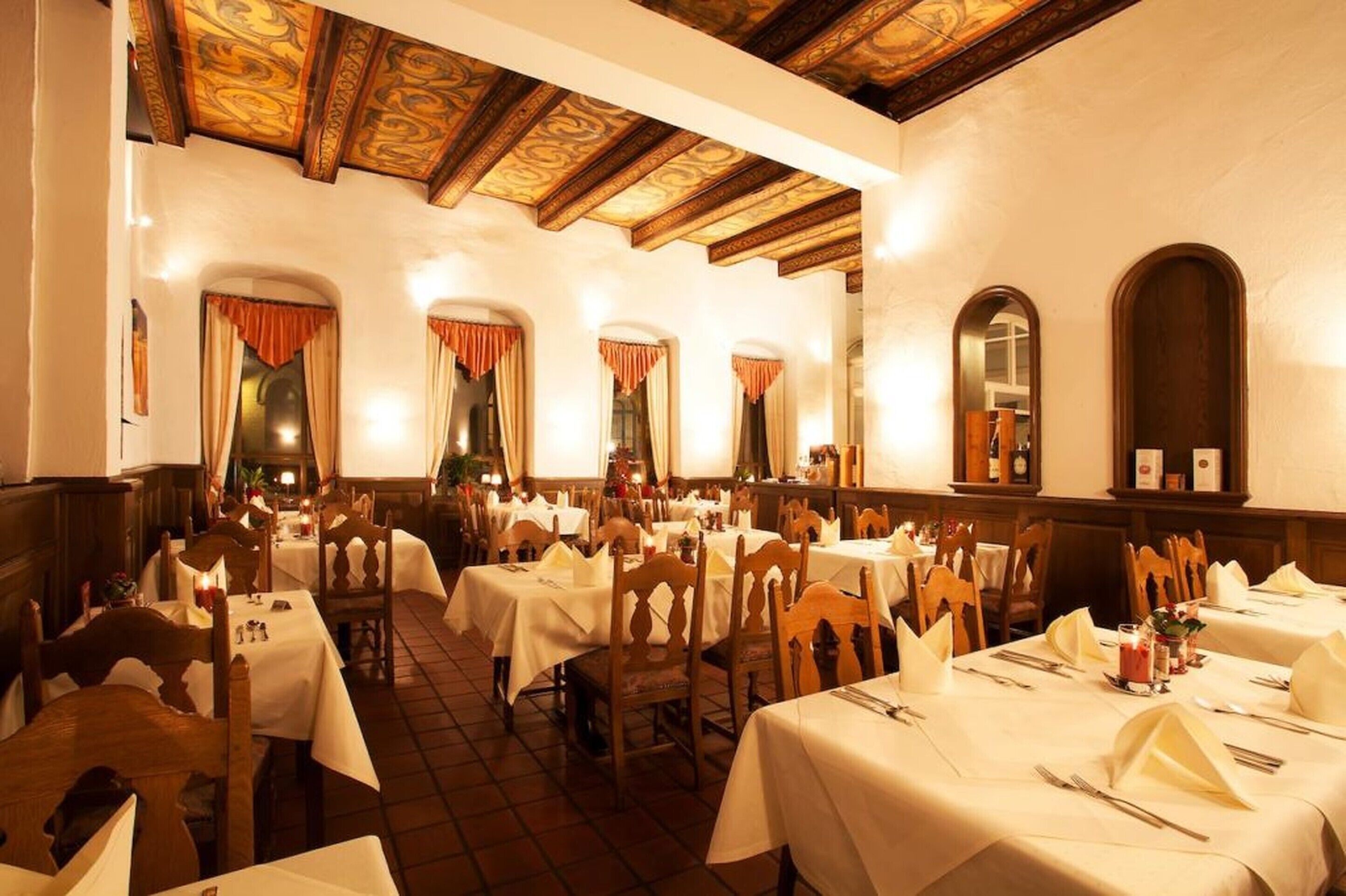 Un restaurante con varias mesas, sillas de madera y piso de baldosas.