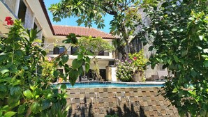 A courtyard with a swimming pool, surrounded by lush greenery and a building with a tiled roof.