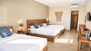 A hotel room with three wooden beds, a wooden desk, a TV, and an air conditioning unit.
